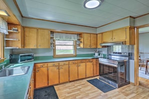 Kitchen area with a window, microwave, stove, and sink.
