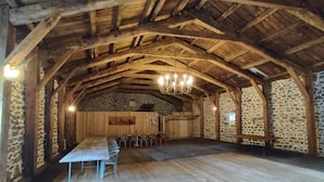Een rustieke houten hal met een hoge plafond, stenen muren en een lange tafel met stoelen.
