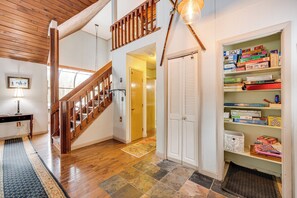 A staircase with wooden railings leading to a second floor, a bookshelf filled with board games, and a patterned rug on the floor. - Rustic Intervale Hideaway w/ Deck & Wooded Views! (Intervale)