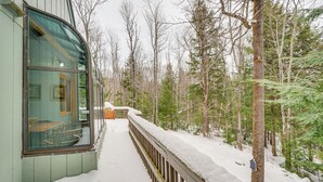 Ein mit Schnee bedeckter Balkon mit Holzgeländer, umgeben von Bäumen.