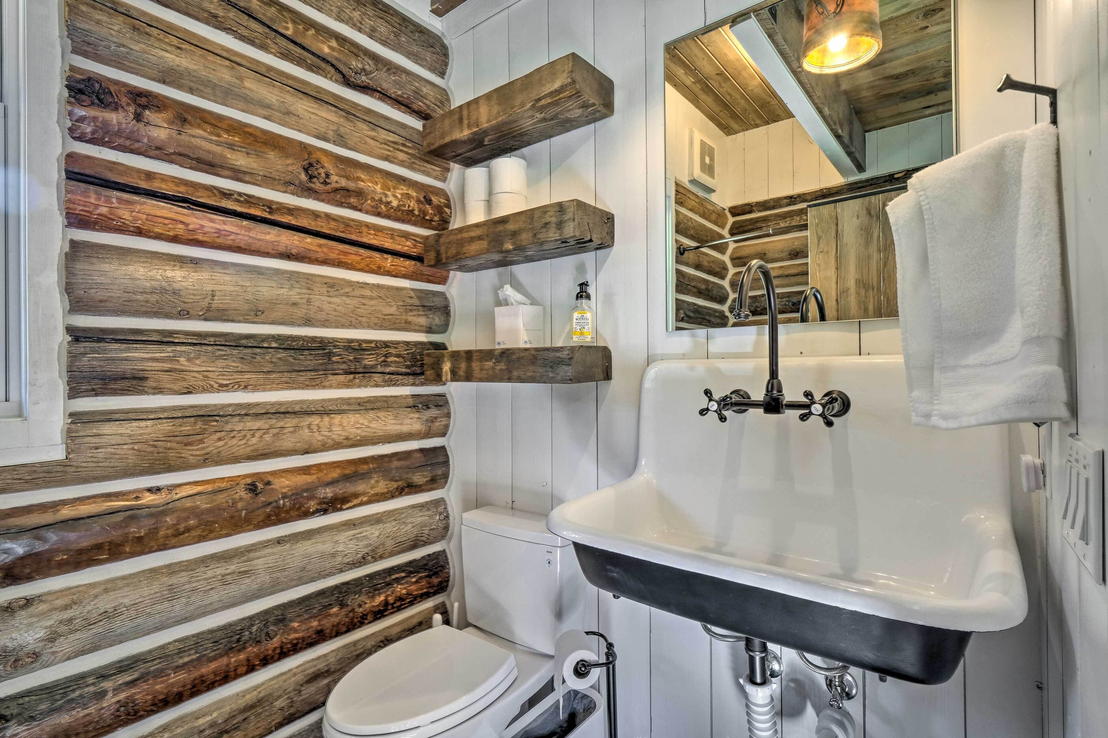 A rustic bathroom with wooden wall paneling, a white toilet, a black sink, and a mirror above the sink.