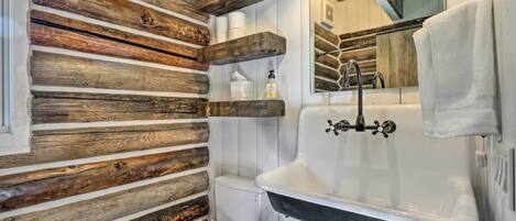 A rustic bathroom with wooden wall paneling, a white toilet, a black sink, and a mirror above the sink.