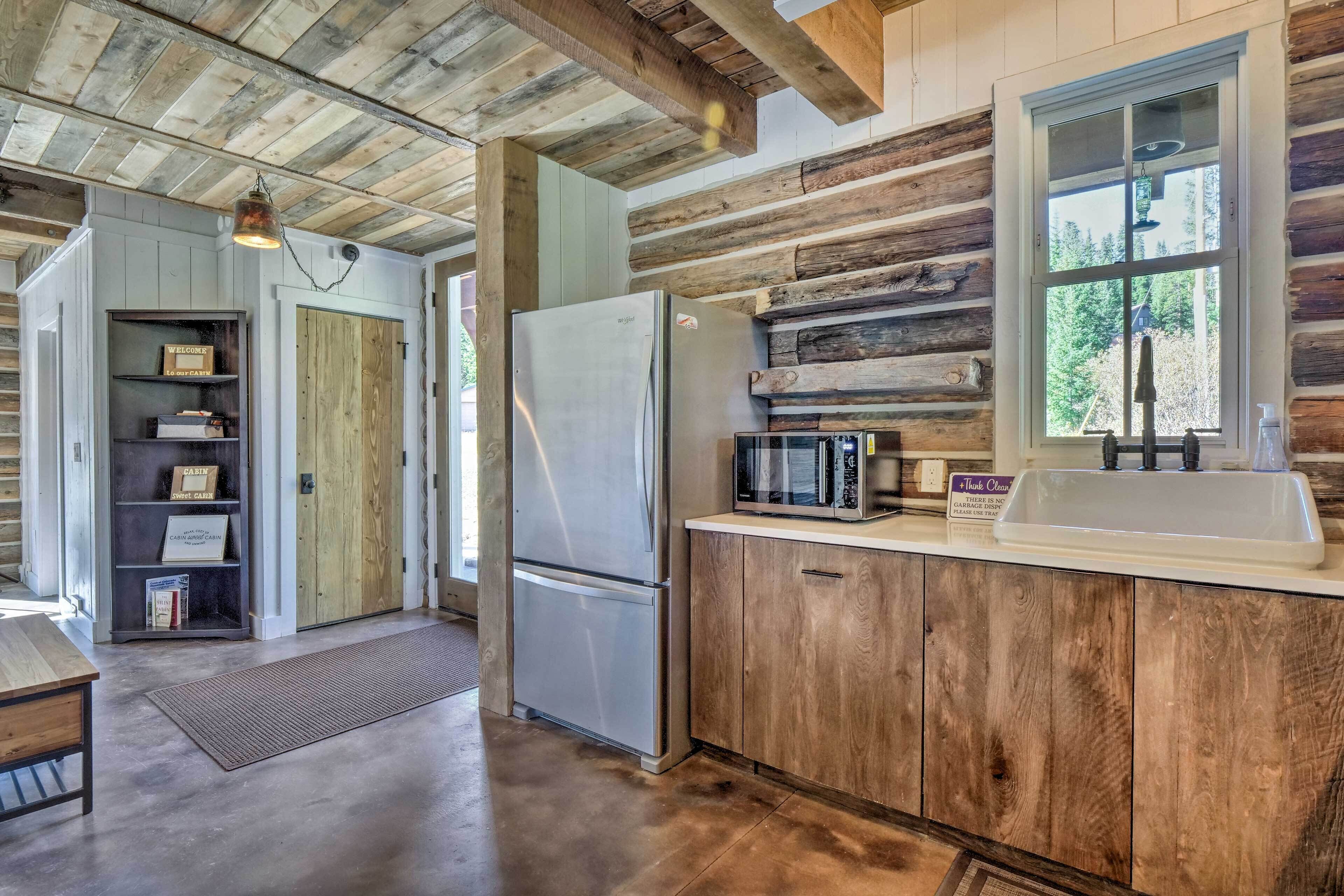 A rustic kitchen with wooden walls, a stainless steel refrigerator, a microwave, and a sink.