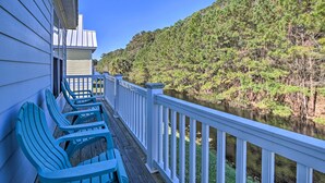 Une terrasse en bois avec des chaises bleues et une balustrade blanche, donnant sur une rivière et une colline boisée.