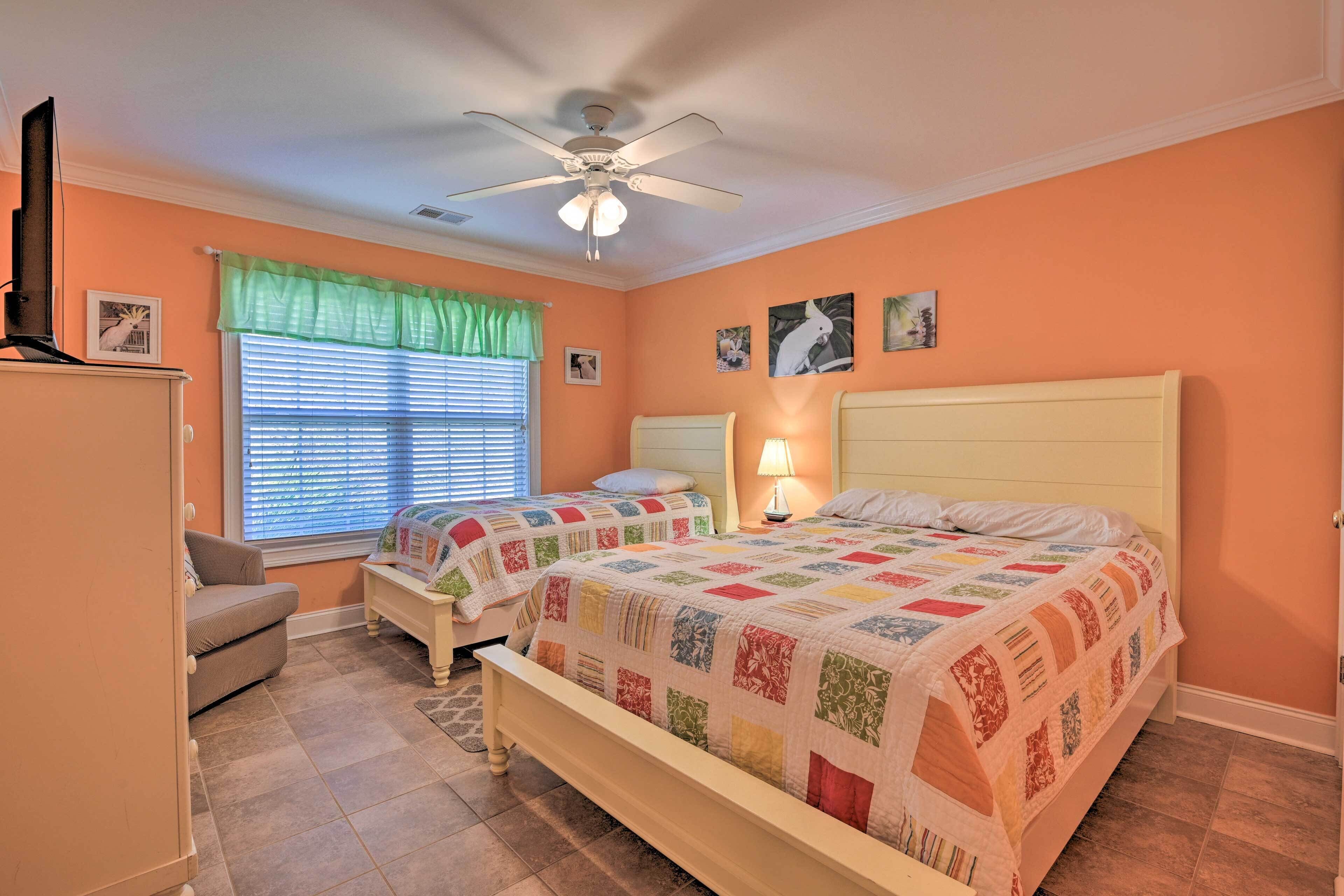 A bedroom with two beds, a ceiling fan, a window with blinds, and a small table.