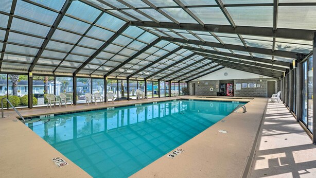 Une piscine intérieure avec des parois en verre transparent, un sol carrelé et une structure de toit.