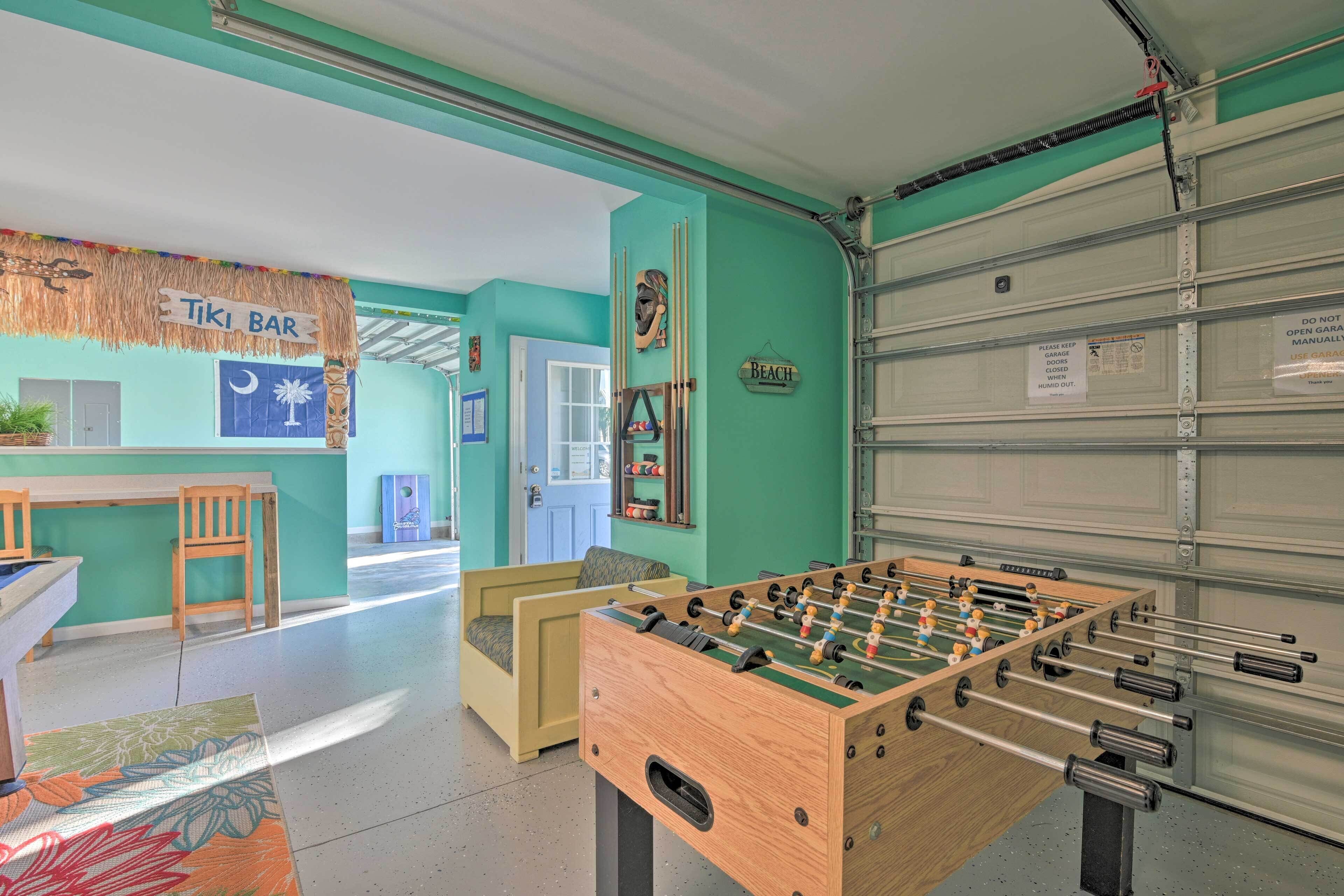 A room with a foosball table, a bar area labeled 'Tiki Bar', and a garage door with a sign indicating it is not to be opened manually.