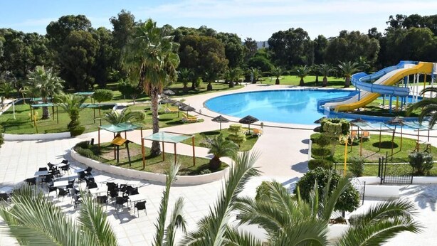 A swimming pool with a water slide, surrounded by palm trees and outdoor seating areas.