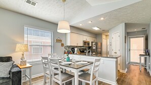 A modern kitchen with white cabinetry, a central island, and a dining area with white chairs and a table set for four.