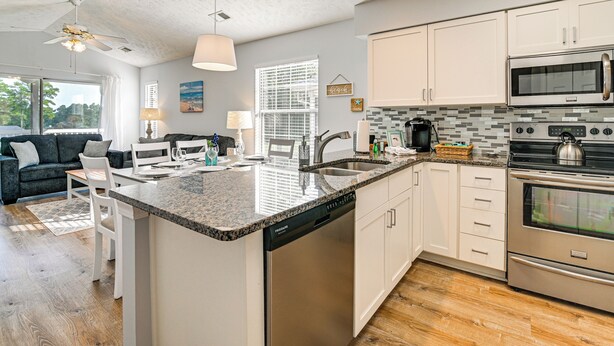 A modern kitchen with white cabinetry, a granite countertop, stainless steel appliances, and a dishwasher.