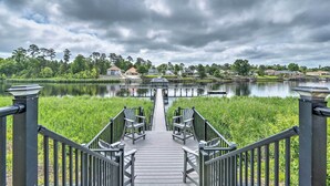 A wooden pier leading to a calm lake with houses in the background.