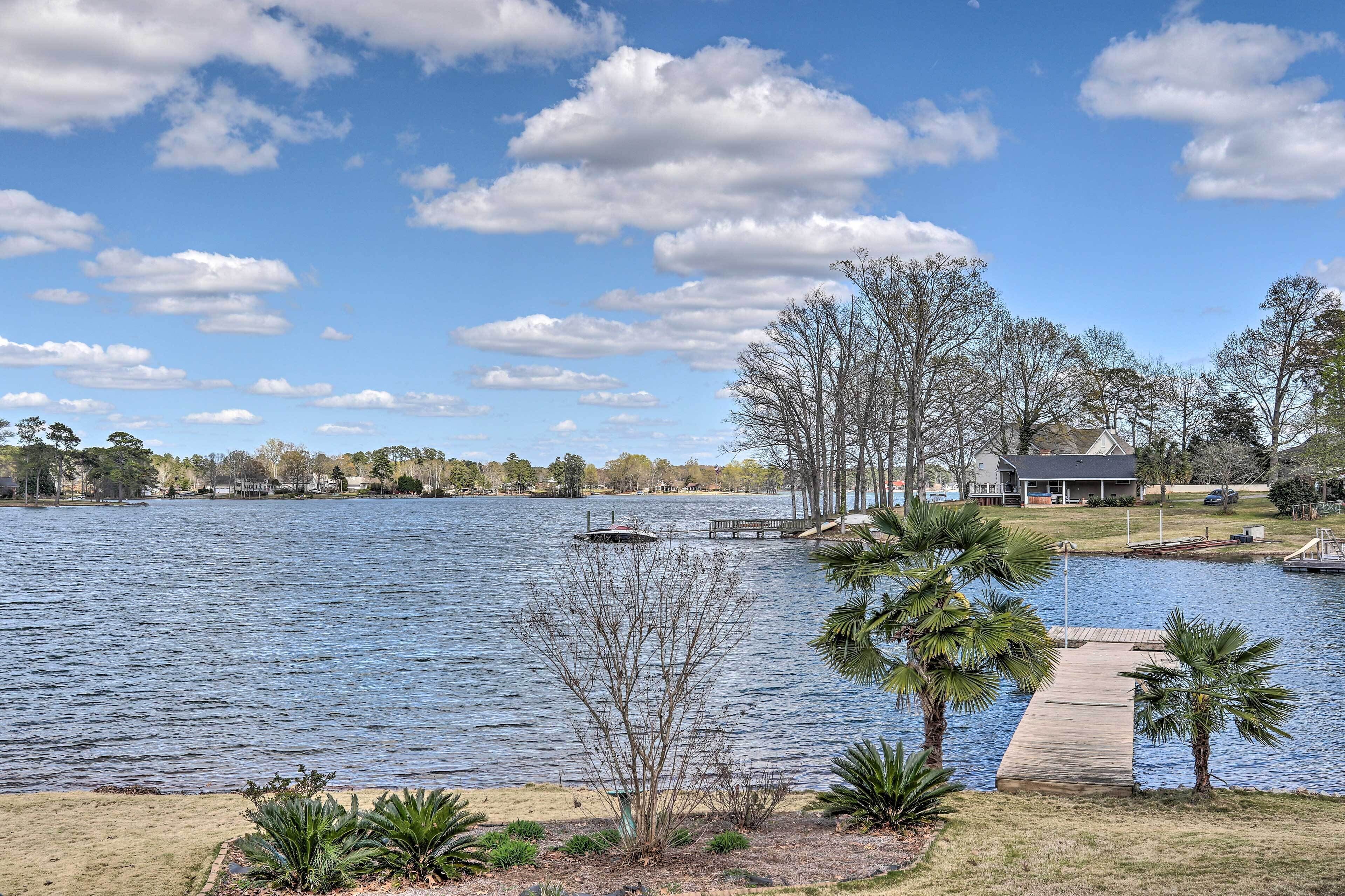 A lake with a dock, palm trees, and a house in the background.