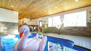 Piscina interna com um brinquedo inflável de cisne, boia de arco-íris e vista do exterior por grandes janelas.