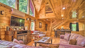 Interior de uma cabana de tronco com sala de estar, área de jantar e escada.