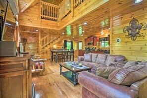 Interior de uma cabana de madeira com área de jantar, cozinha e escada para um andar superior.