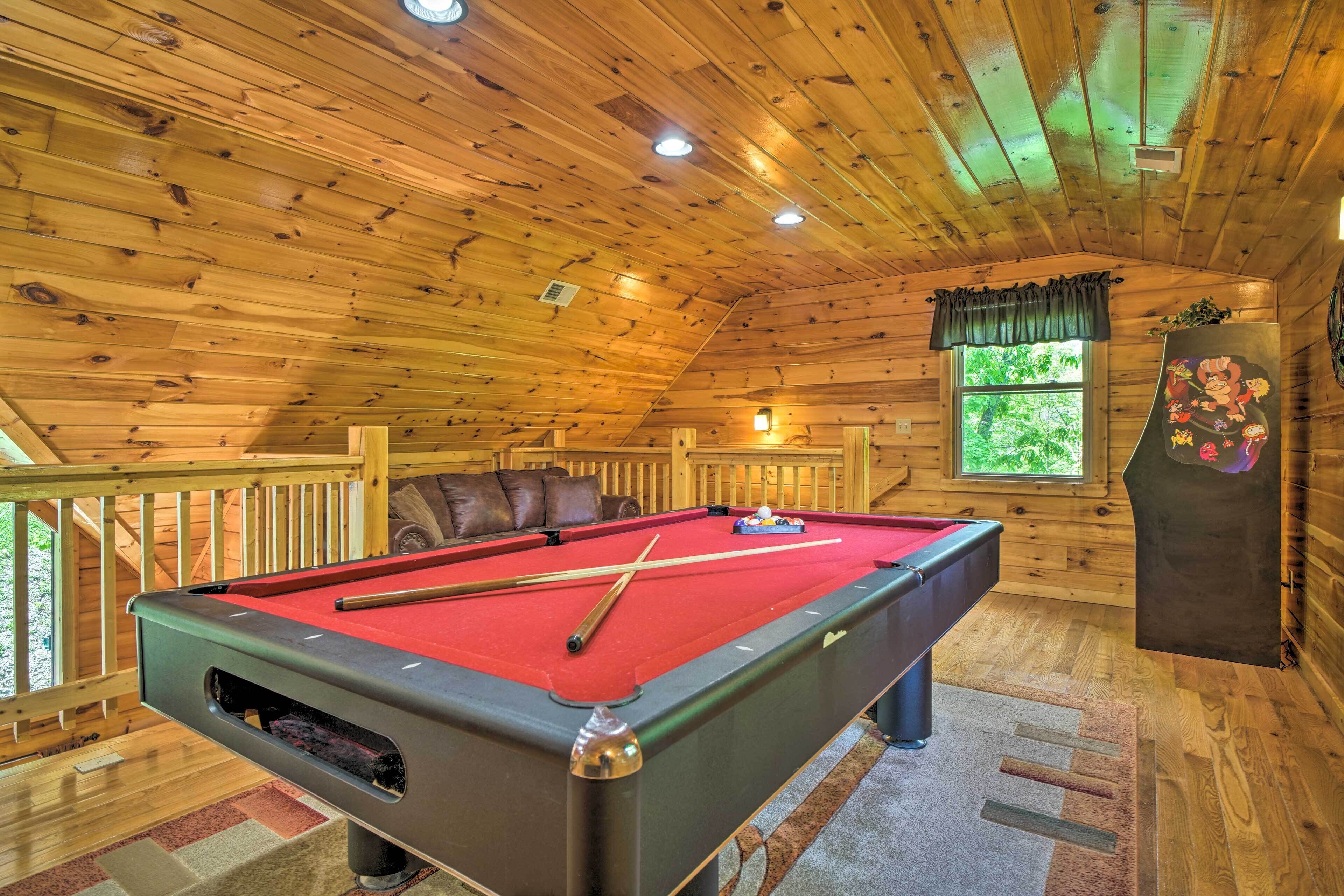 Un intérieur en bois avec une table de billard, un banc rembourré et une fenêtre donnant sur un paysage verdoyant.
