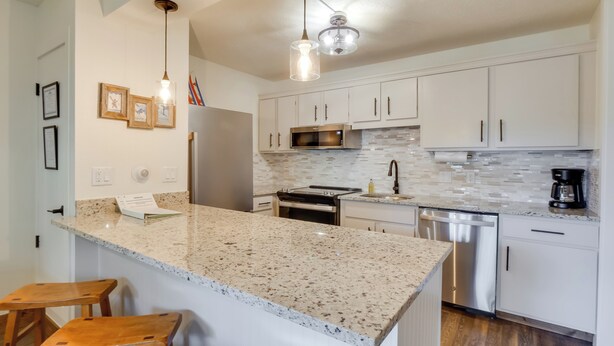 A modern kitchen with granite countertops, stainless steel appliances, and white cabinetry. - Walk to Ski Shuttle: Cozy Mountain Meadows Condo (Frisco)