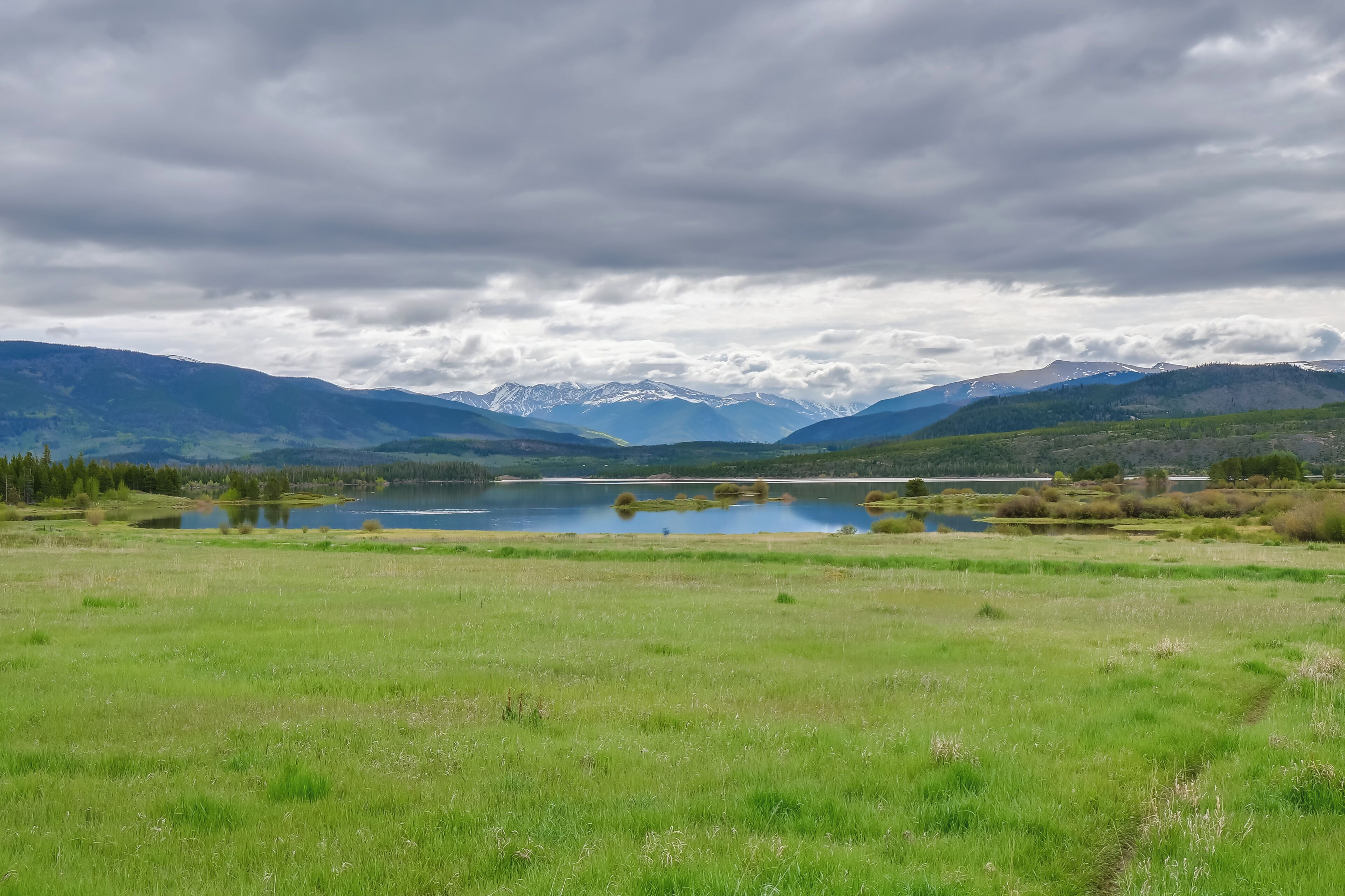 A panoramic view of a mountainous landscape with a lake and fields.