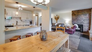 A modern kitchen with white cabinets, a stone backsplash, and a wooden dining table with a vase. - Walk to Ski Shuttle: Cozy Mountain Meadows Condo (Frisco)