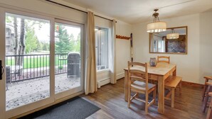 A dining area with a wooden table and chairs, a chandelier, and a view of a backyard with a grill and trees. - Walk to Ski Shuttle: Cozy Mountain Meadows Condo (Frisco)