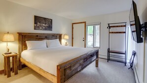A bedroom with a wooden bed, bedside lamps, a mounted TV, and a window with a view of greenery. - Walk to Ski Shuttle: Cozy Mountain Meadows Condo (Frisco)