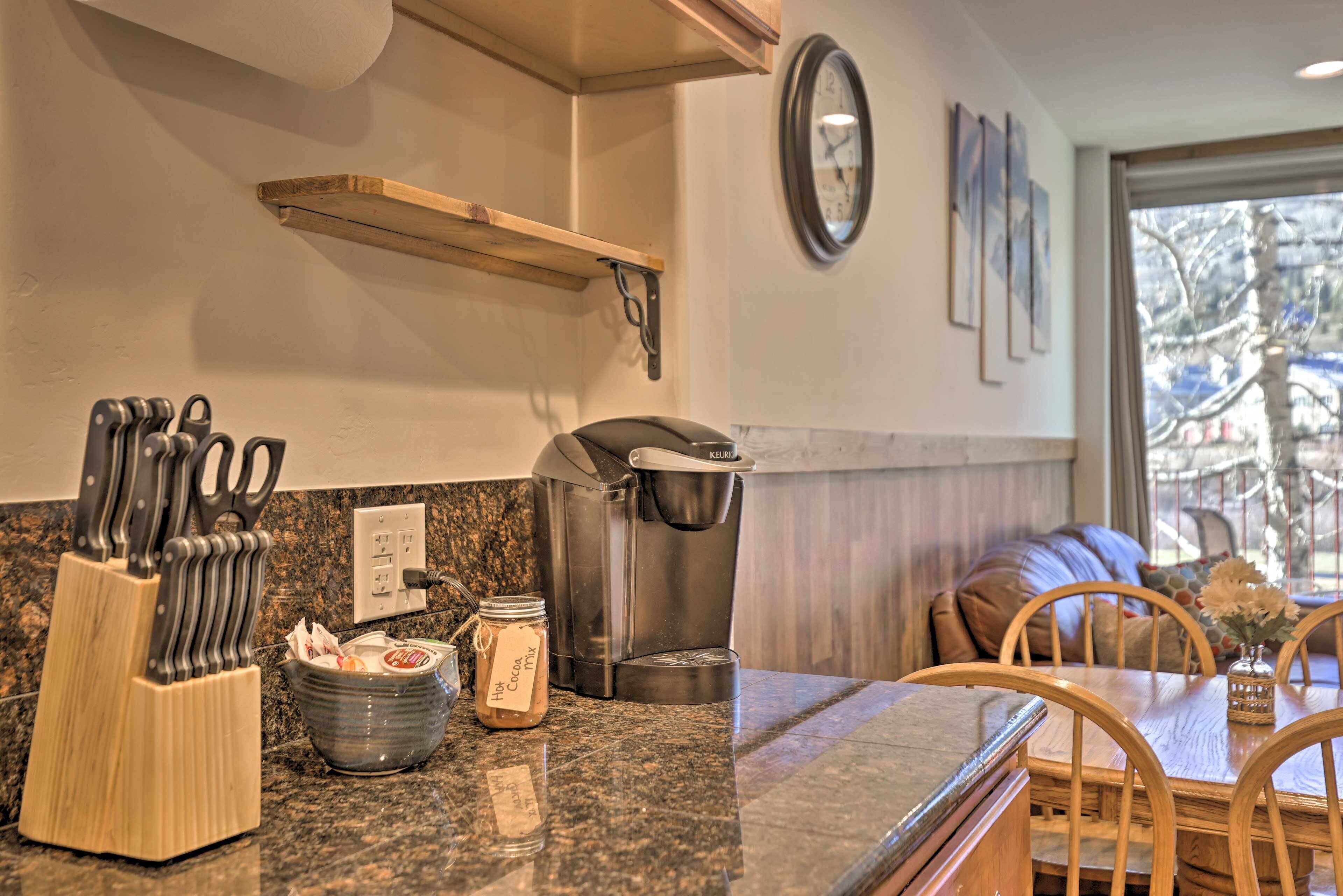 Una cocina con cafetera, bloque de cuchillos y un tarro de mezcla para chocolate caliente.