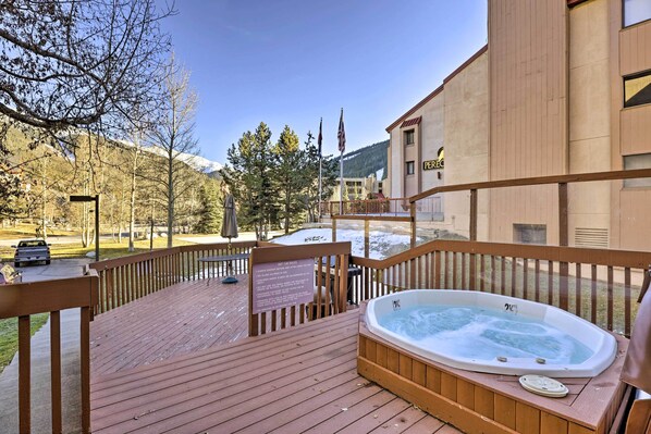 A wooden deck with a hot tub, a sign, and a view of a mountain and trees. - Copper Mountain Condo Near Ski Lift & Golf Course! (Copper Mountain)