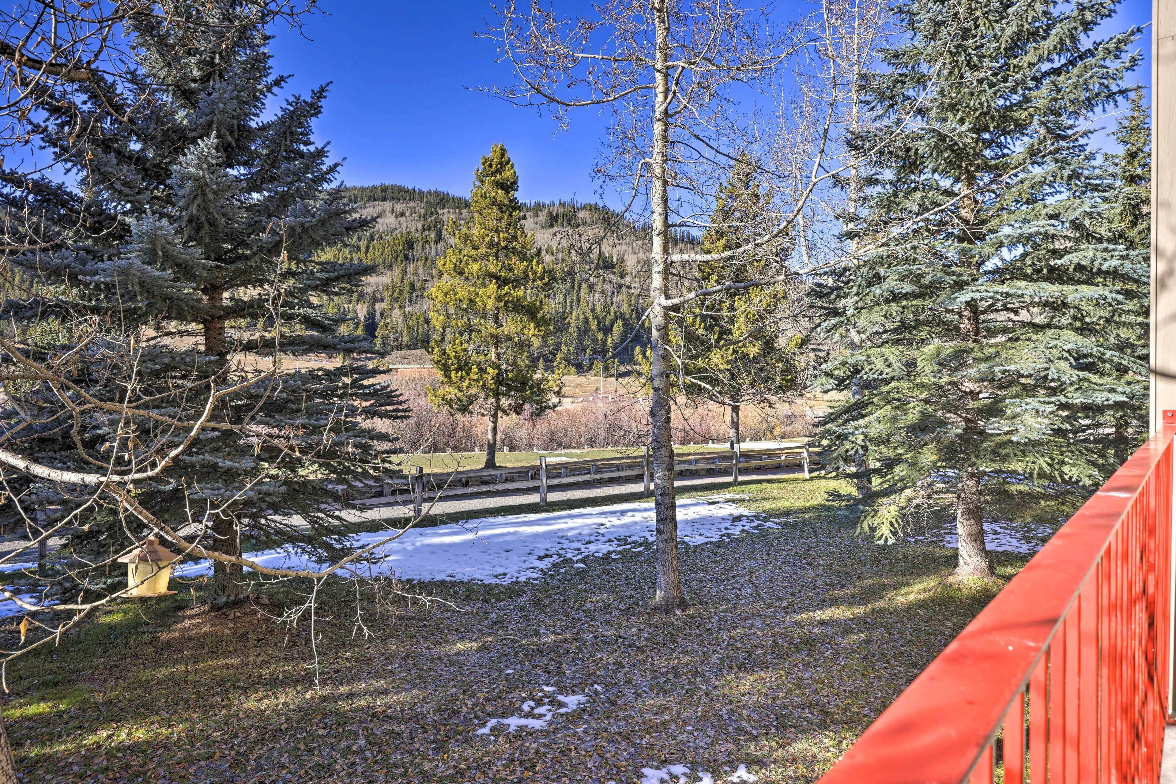 A view of a forested area with a wooden deck and a red railing.