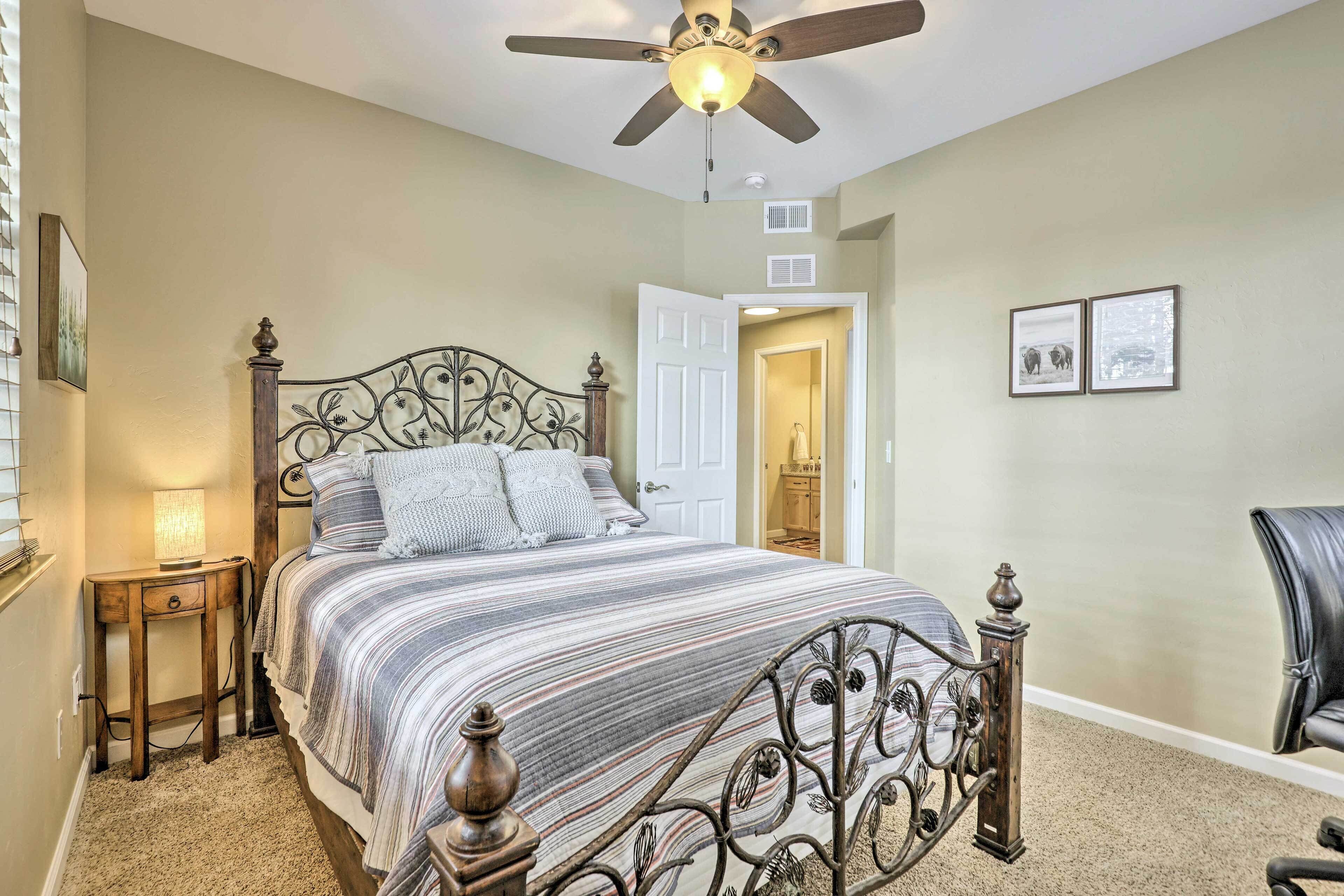 A bedroom with a bed, a ceiling fan, a nightstand, a chair, and a door leading to another room.