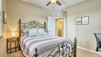 A bedroom with a bed, a ceiling fan, a nightstand, a chair, and a door leading to another room.