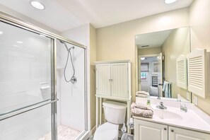 A bathroom with a glass shower enclosure, a toilet, a sink with a mirror, and a cabinet.