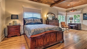 A bedroom with a wooden ceiling, a large bed with a patterned bedspread, a dresser, a chair, and a desk with a mirror. - Spacious & Updated 1920's Hsnp Craftsmen Home (Hot Springs)