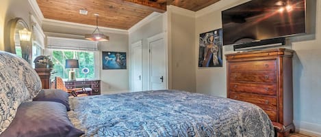 A bedroom with a large bed, wooden ceiling, a dresser, a television, and artwork on the walls.