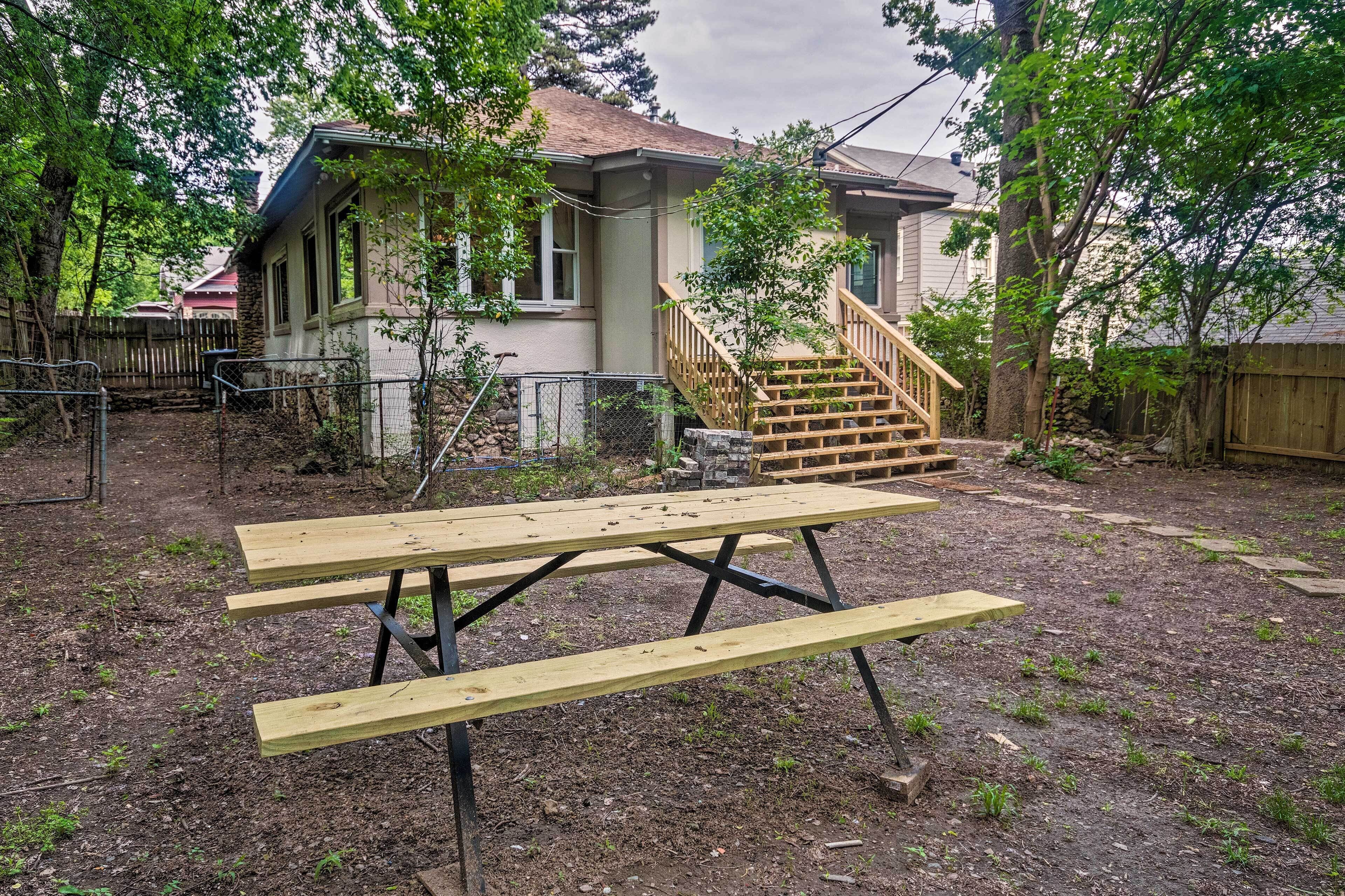 A backyard with a wooden picnic table, a wooden staircase, and a house with a fenced yard.