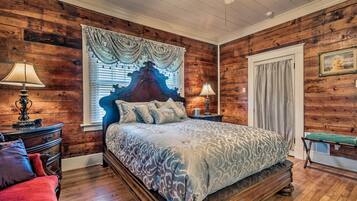 Une chambre aux murs lambrissés, avec un grand lit, deux tables de chevet et une fenêtre avec des rideaux.