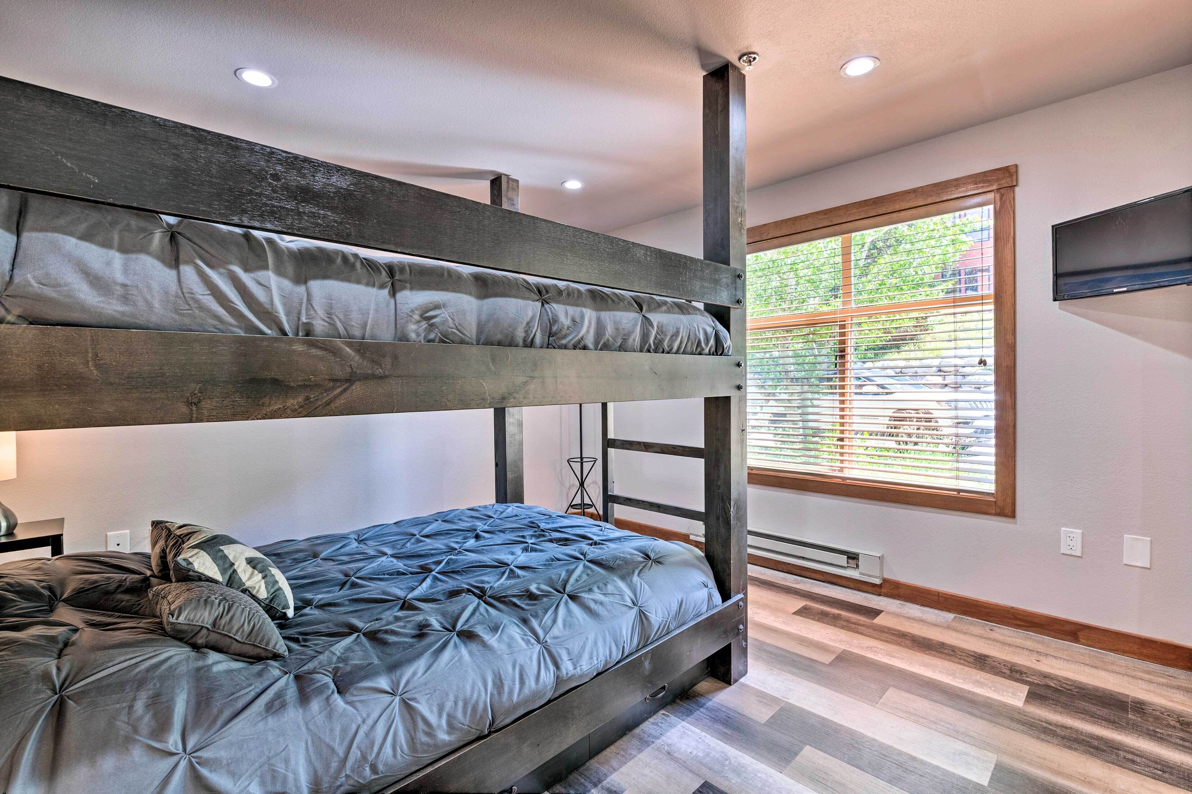 A bunk bed room with a window, wooden flooring, and a TV mounted on the wall.