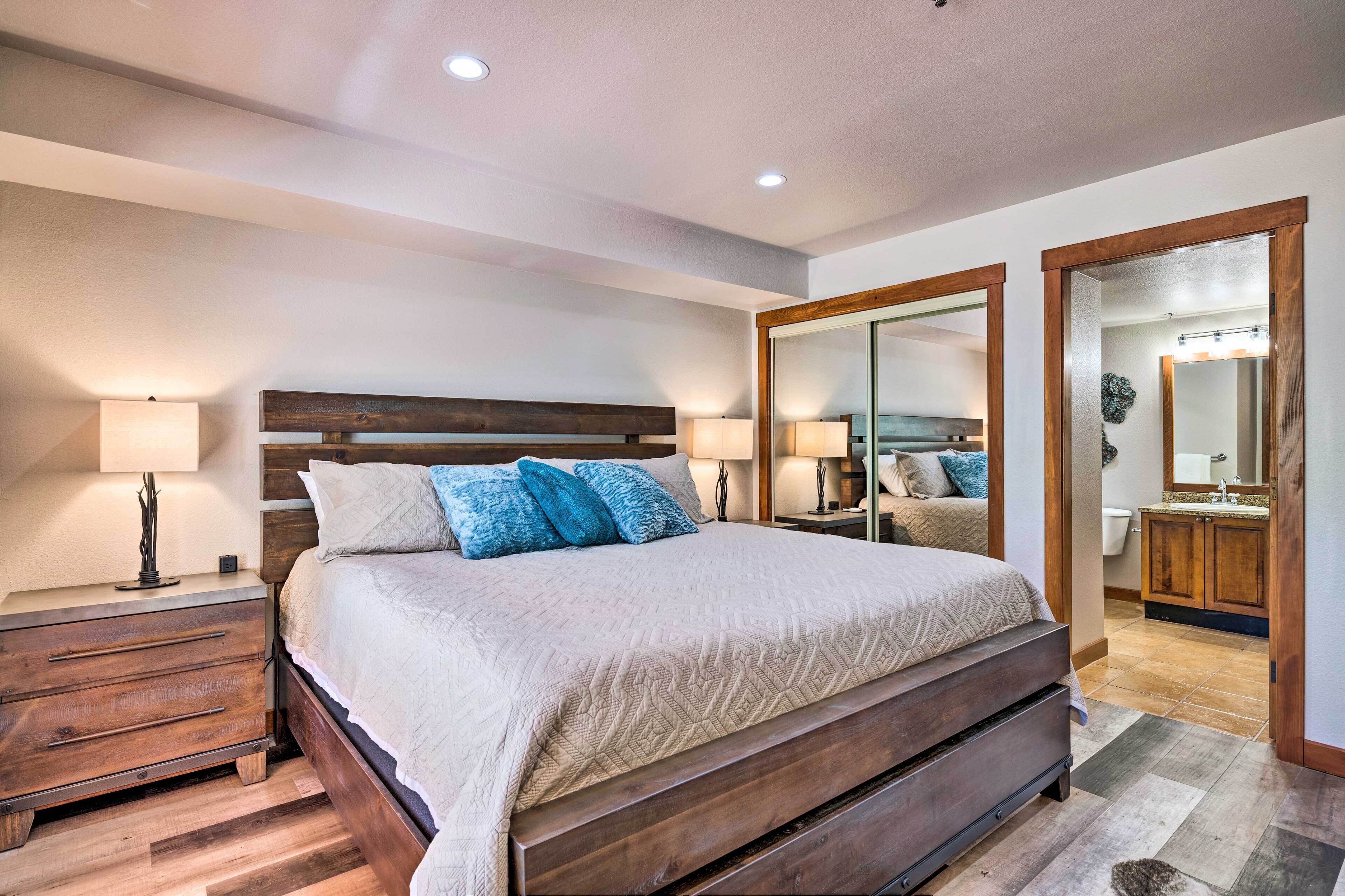 A bedroom with a wooden bed, two bedside tables with lamps, a large mirror, and a view into the bathroom.
