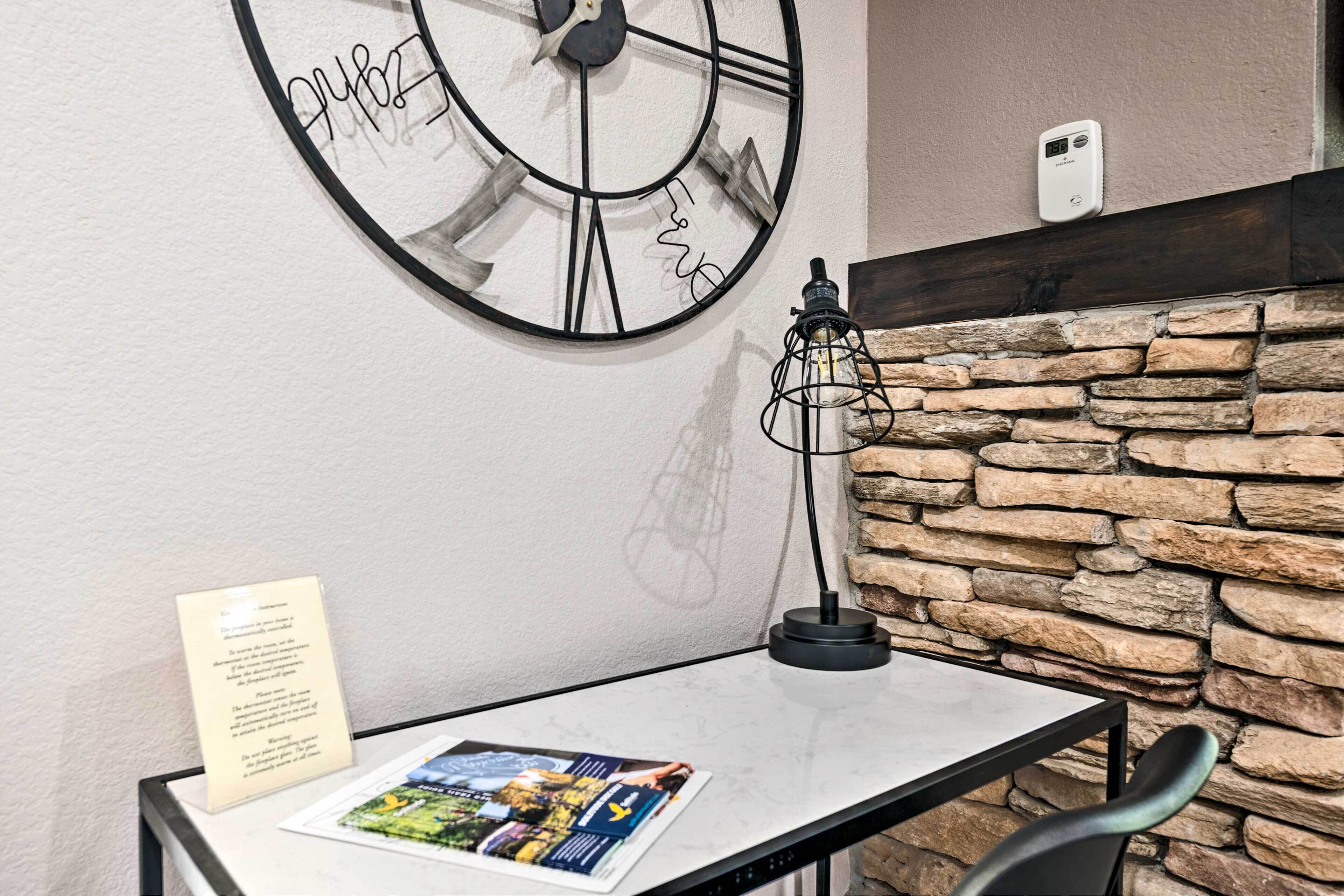 A hotel room with a stone wall, a large clock, a table with a lamp, and a sign on the wall.