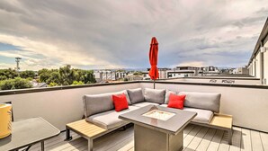 Una terraza en la azotea con un sofá seccional gris, una mesita y un paraguas rojo.