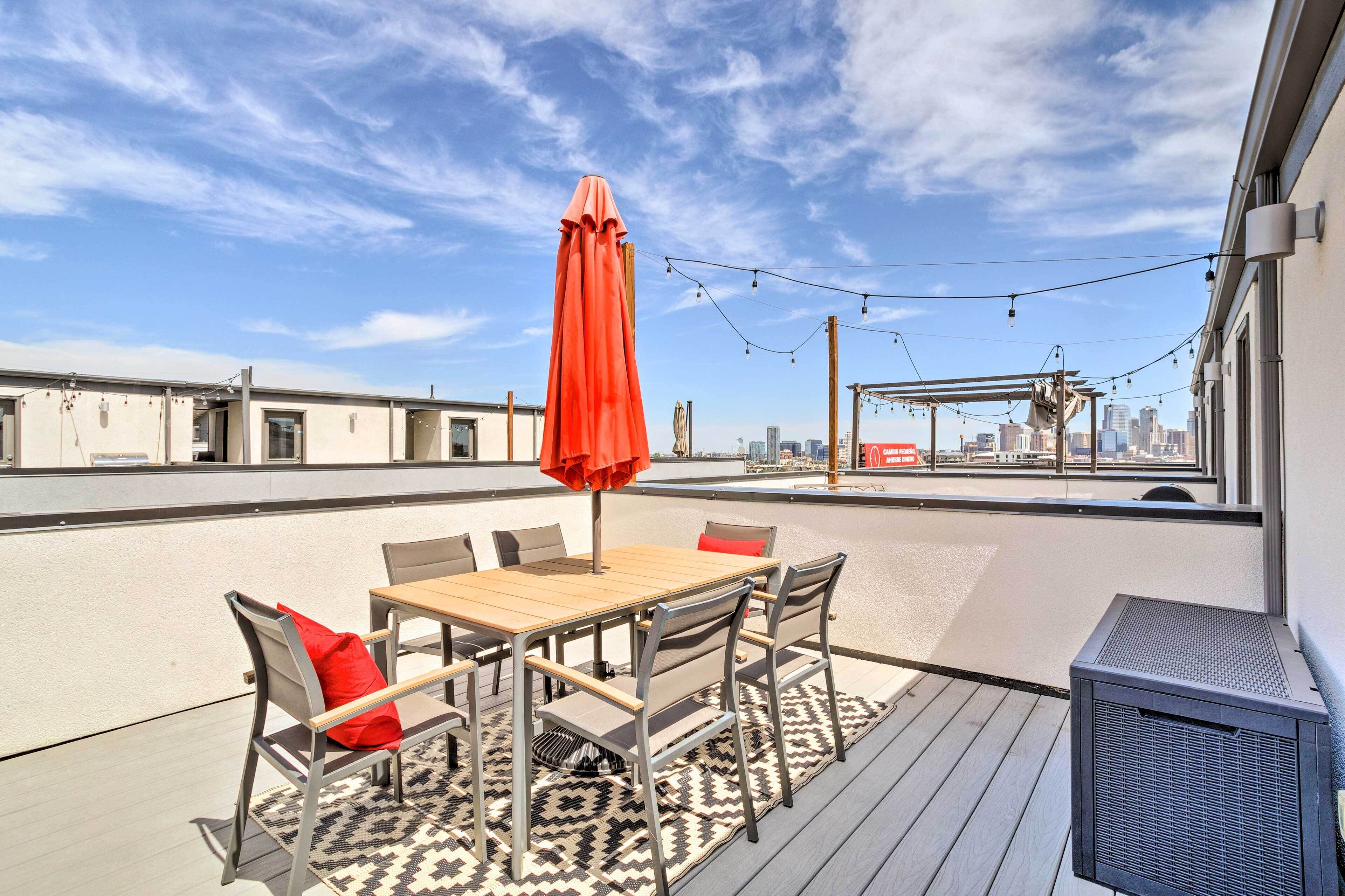 An outdoor patio with a wooden table and chairs, a red umbrella, and a patterned rug.