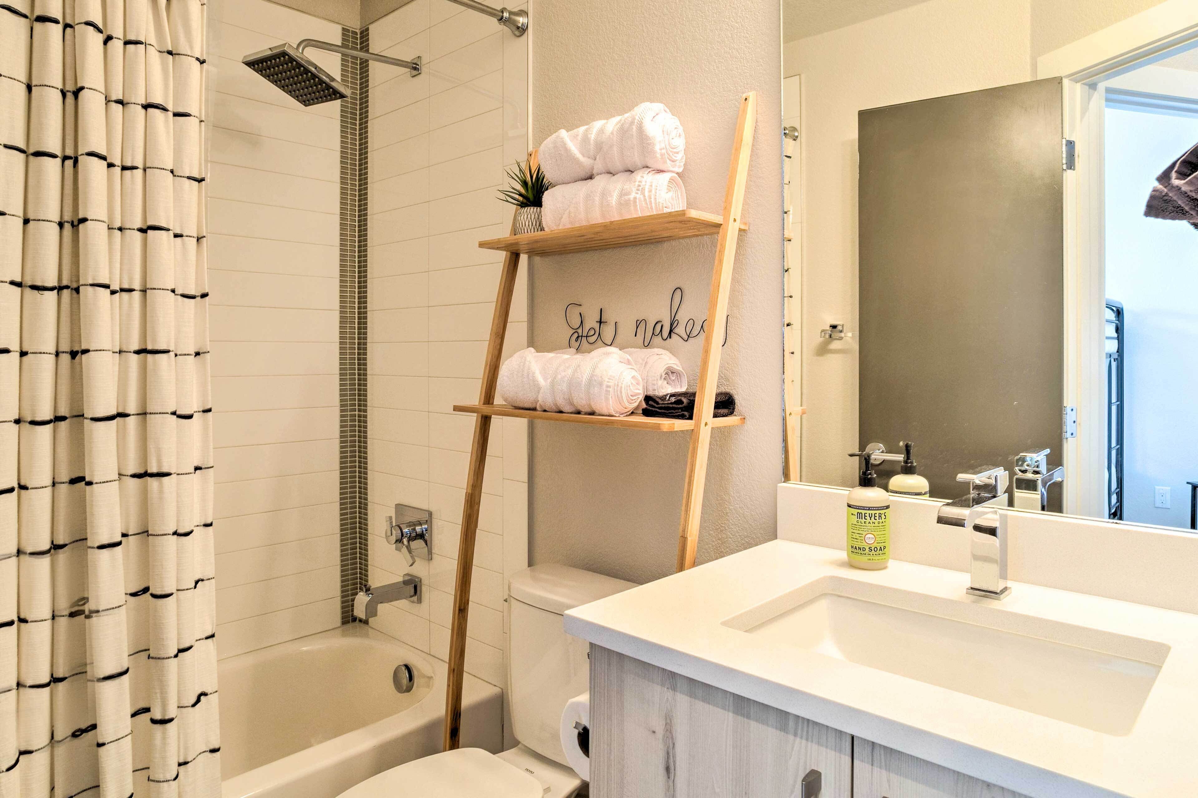 A bathroom with a bathtub, toilet, and a wooden shelf holding towels.