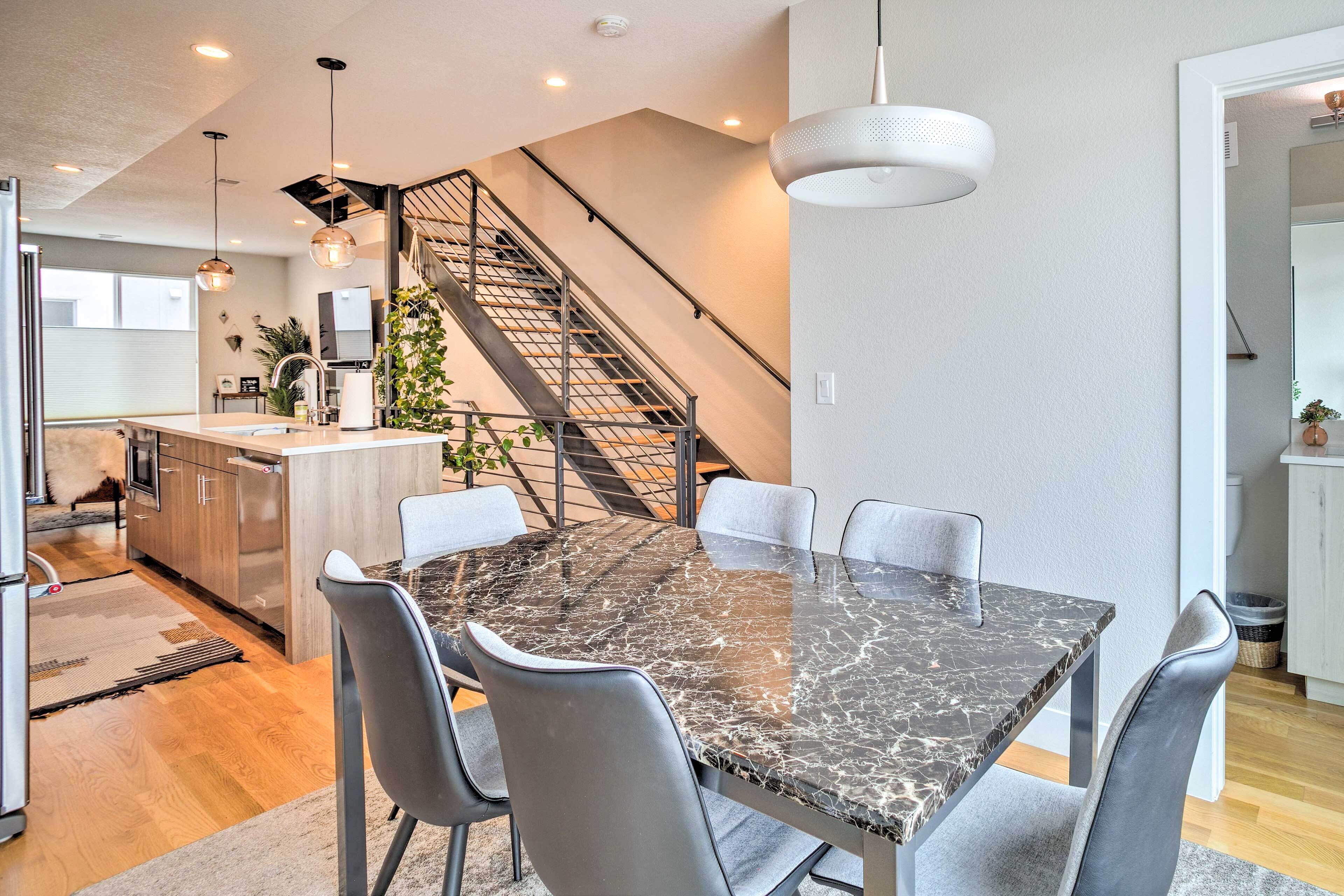 A modern kitchen with a marble island, grey chairs, and a staircase leading to an upper level.