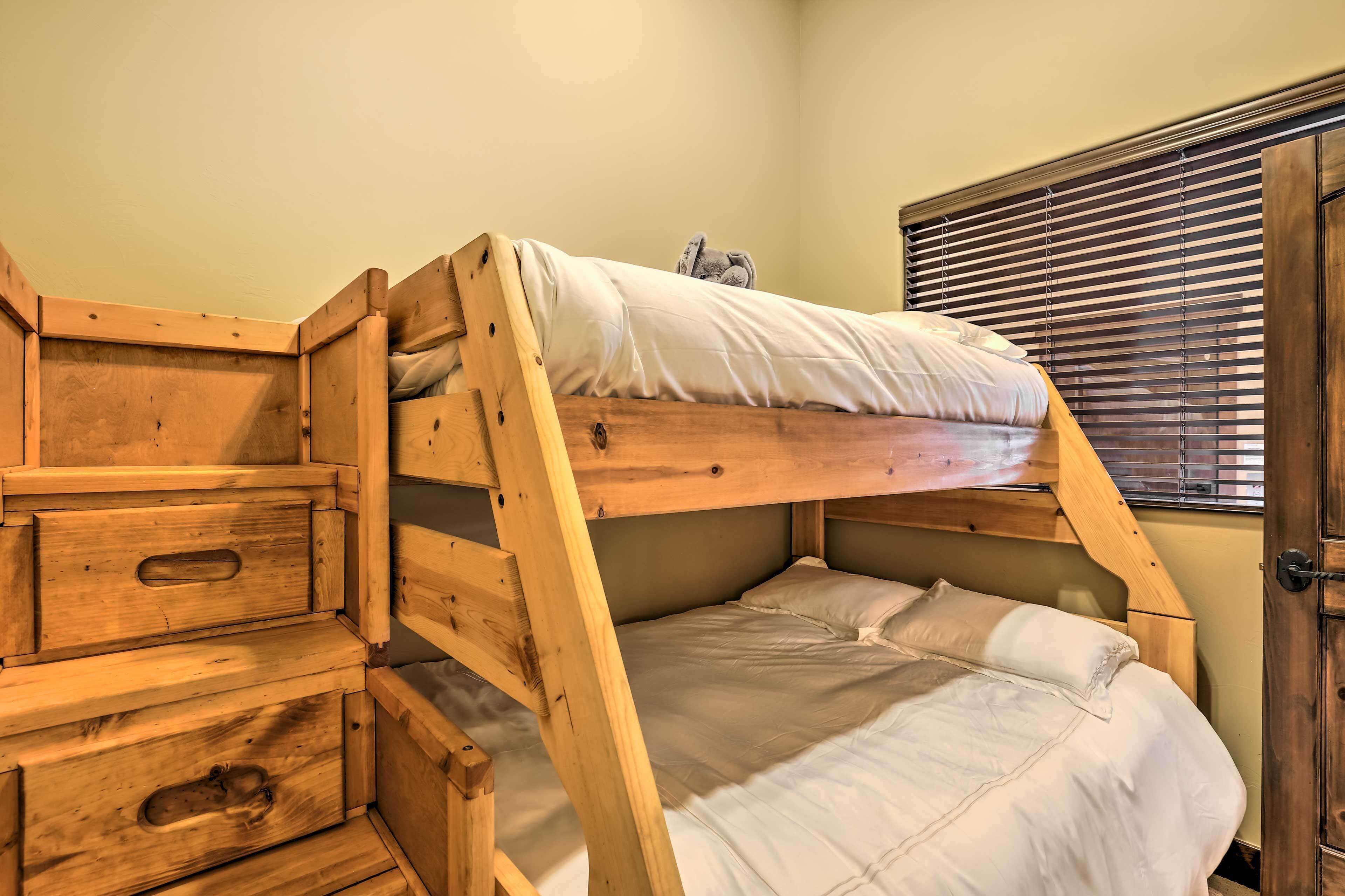 Un lit superposé avec des tiroirs en bois et une fenêtre équipée de stores.
