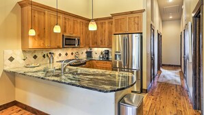 Une cuisine dotée de meubles en bois, d’un plan de travail en granit, d’appareils électroménagers en acier inoxydable et de luminaires suspendus.