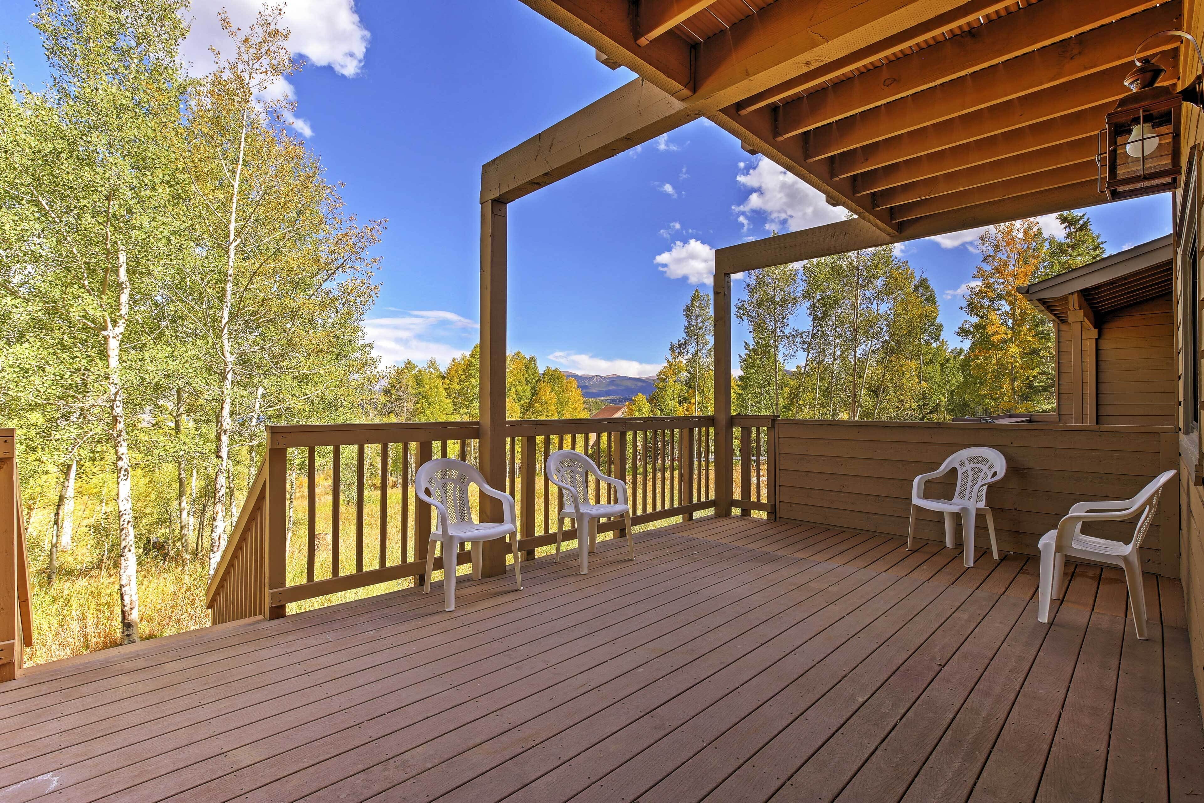 A wooden deck with four white plastic chairs, a wooden railing, and a view of trees and mountains.
