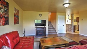 Un salon avec un canapé en cuir rouge, une table basse en bois, une cheminée et un escalier menant à une autre pièce.