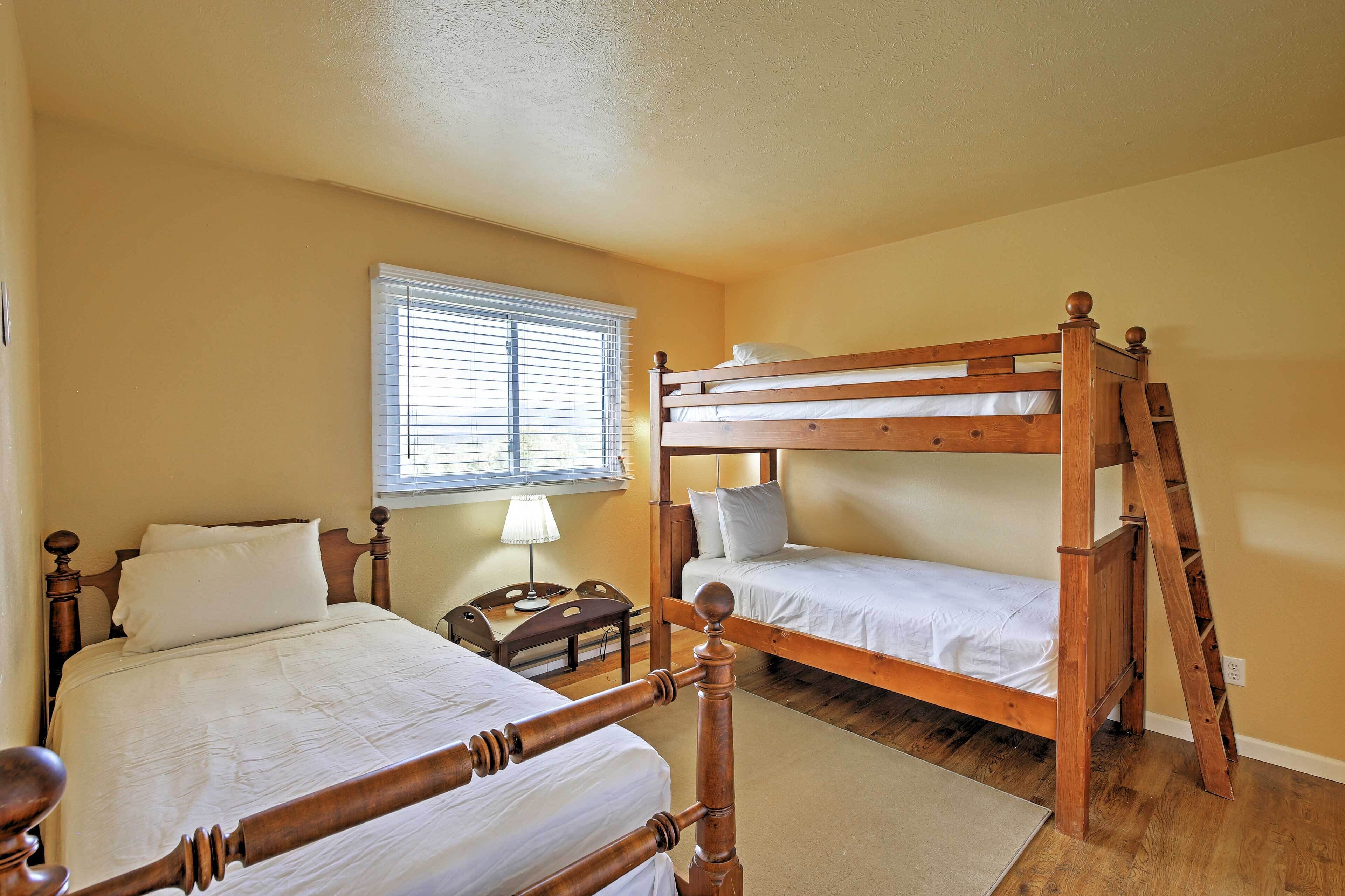 A room with two bunk beds, a small bedside table, a lamp, and a window with blinds.