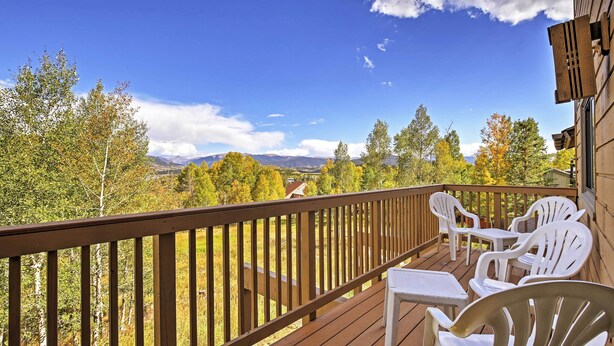 Une terrasse en bois, avec des chaises et une table en plastique blanc, offrant une vue sur un paysage montagneux.