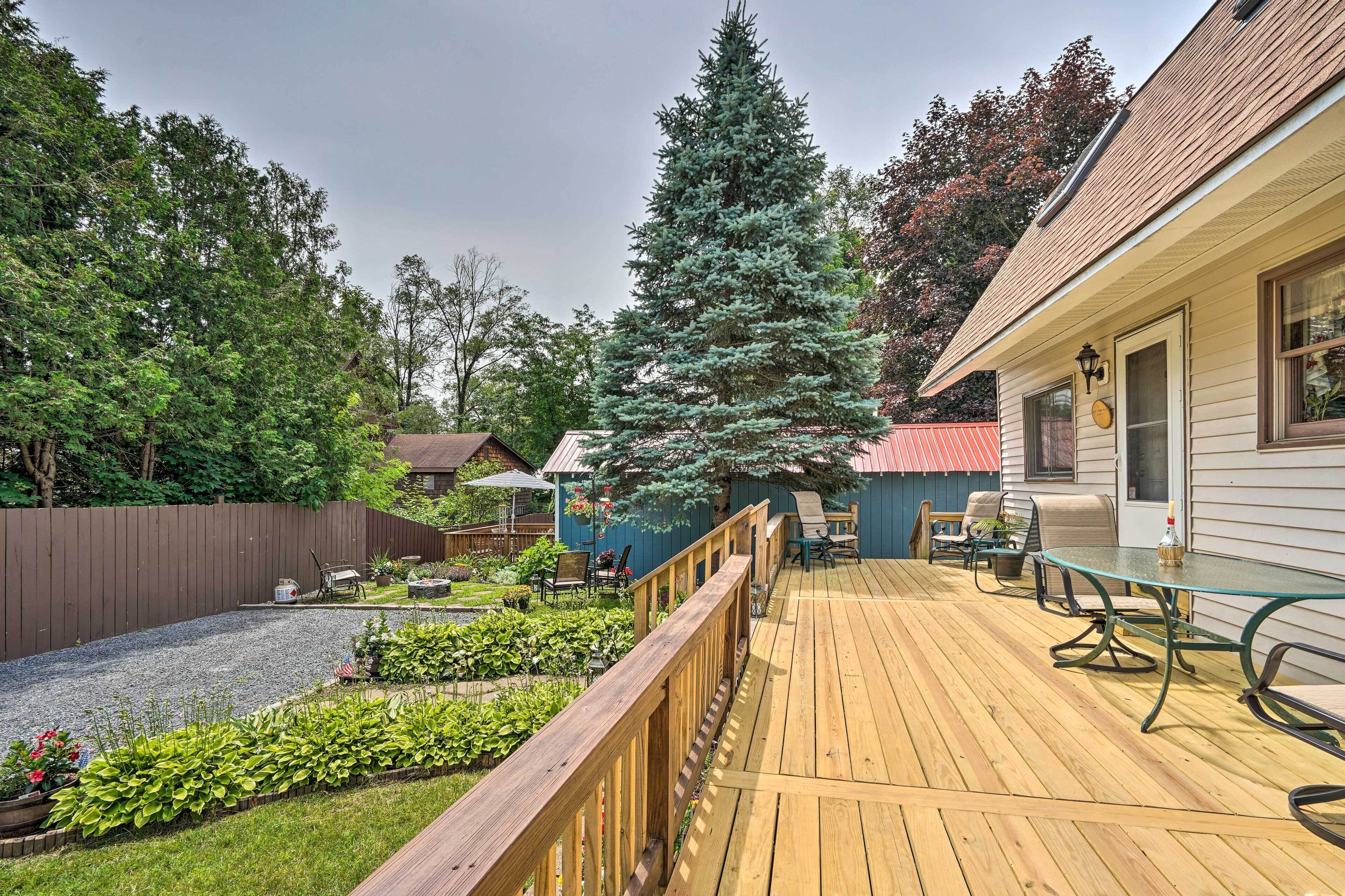 A wooden deck with outdoor furniture, a tall evergreen tree, and a house with a red roof.