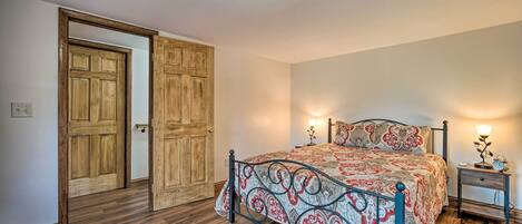 A bedroom with a wooden door, a metal bed frame, a bedside table with a lamp, and a nightstand with a clock.